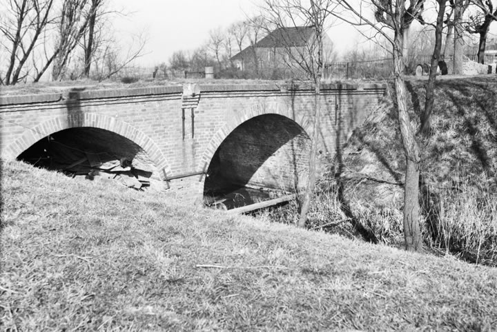 Op bovenstaande foto van de Dienst Cultureel Erfgoed uit maart 1957 is de brug over de borggracht goed te zien. De leuning is dan al gesloopt. Op de achtergrond het kerkje van Lellens. Licentie: Public Domain.