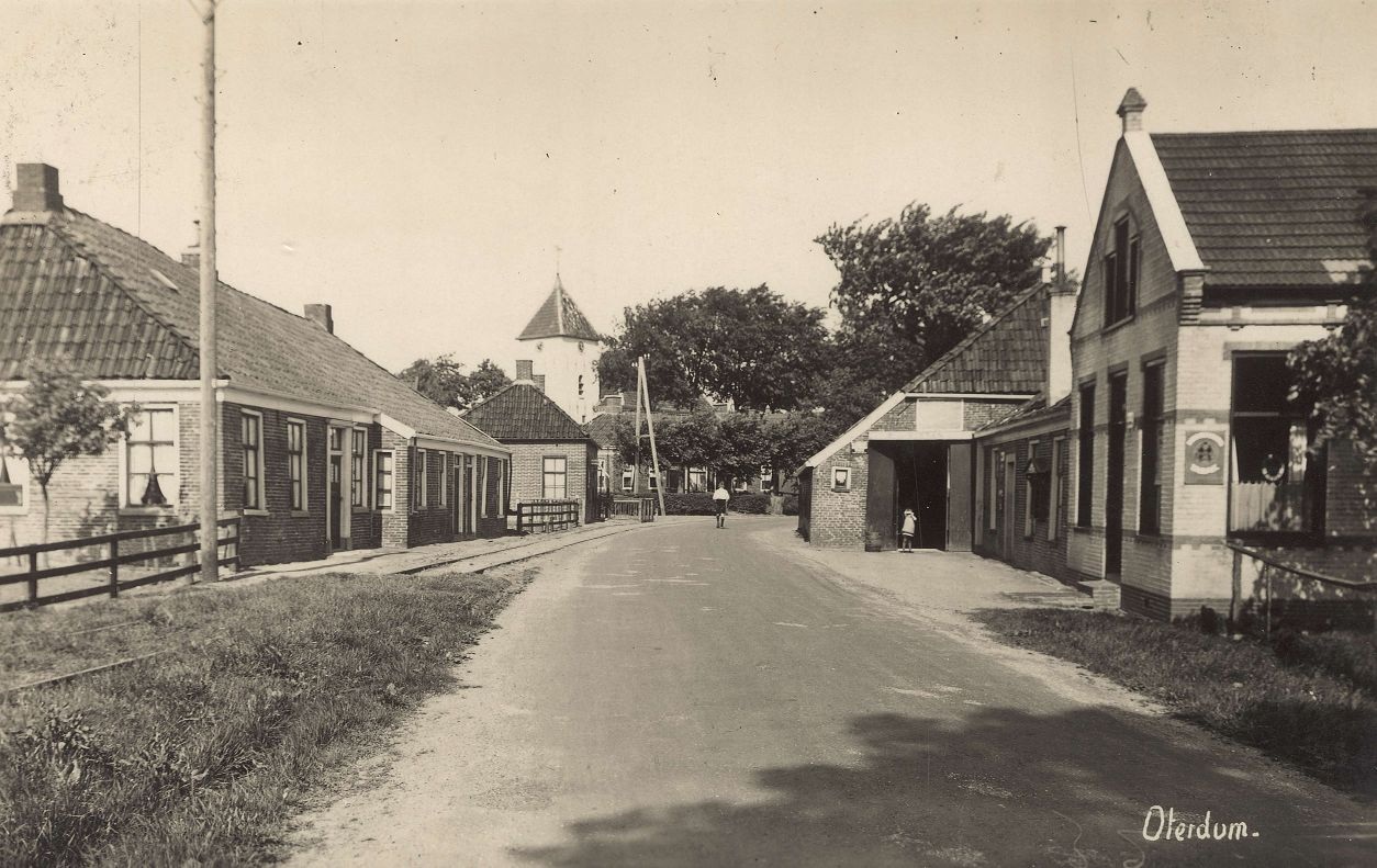 Hoofdstraat van Oterdum rond 1920, met de kerktoren op de achtergrond. Rechts Café de Vries met doorrit, links de trambaan van OG. Bron: RHC GA, Groninger Archieven, Beeldbank Groningen.