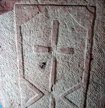 Foto boven: Een bewerkte deel van een grafdeksel met een kruis.