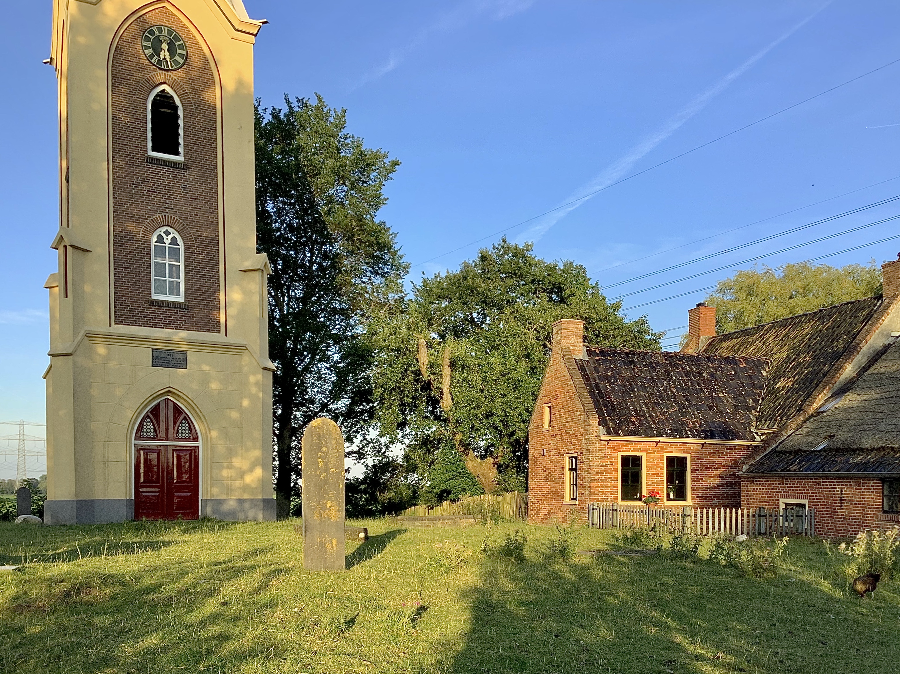 Links de toren en rechts de boerderij naast het kerkhof. Foto: ©Jur Kuipers, Hoogezand, maart 2022.