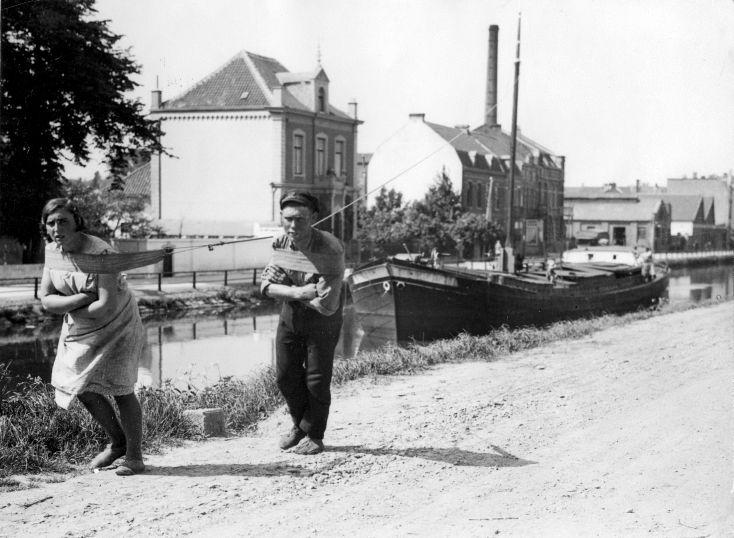 Jagen: trekken van een schuit. Man en vrouw trekken een vrachtschip door een binnenkanaal. Plaats onbekend, 27 mei 1931. Bron: Wikimedia Commons.