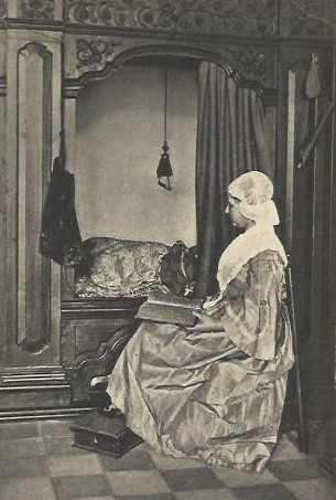 Een vrouw in de Groninger klederdracht voor de bedstee.